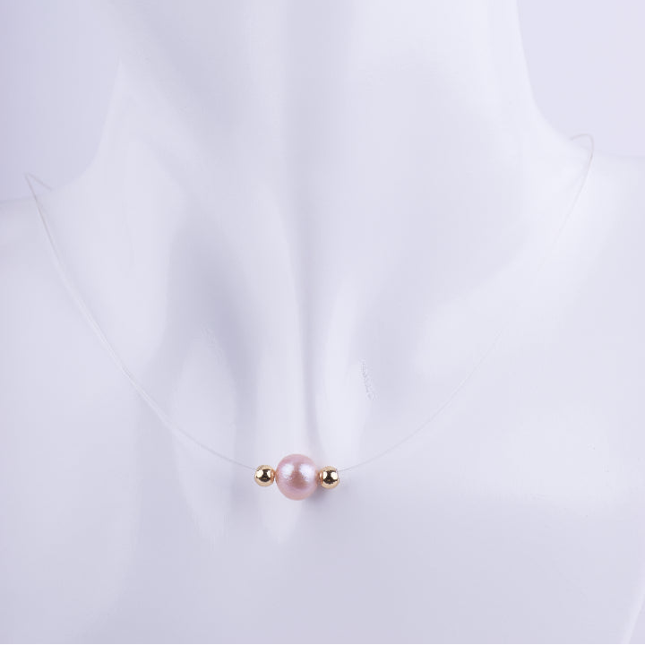 Collar de hilo de nylon transparente con una perla rosada y dos pequeñas esferas doradas, creando la ilusión de que el dije flota sobre el cuello de un maniquí blanco.