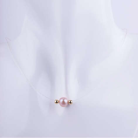 Collar de hilo de nylon transparente con una perla rosada y dos pequeñas esferas doradas, creando la ilusión de que el dije flota sobre el cuello de un maniquí blanco.