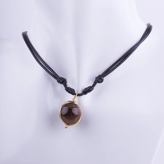 Collar artesanal con esfera de piedra natural Ojo de Tigre envuelta en alambre dorado sobre un cordón negro ajustable estilo amuleto.