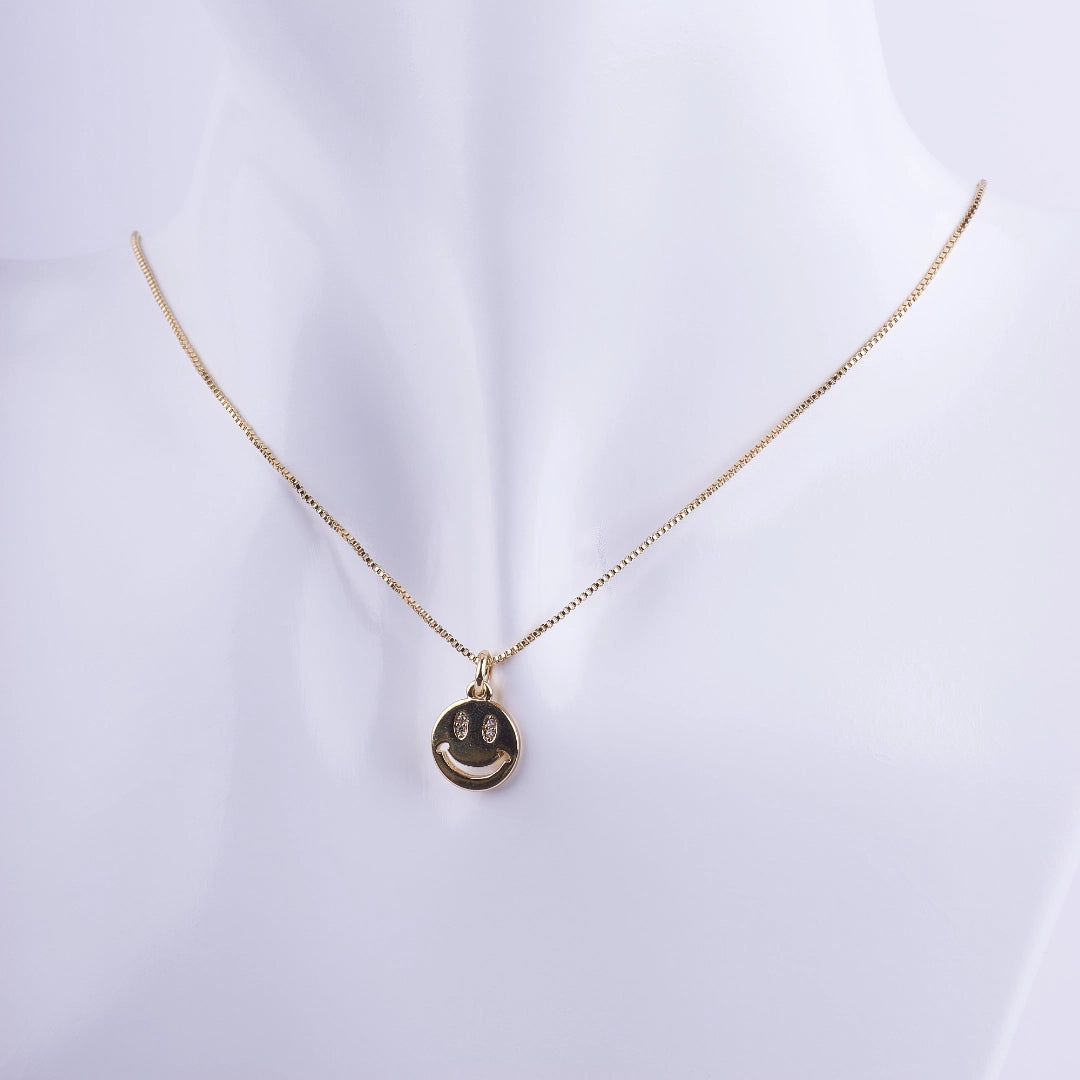 Collar bañado en oro con dije circular de carita feliz (smiley face) con ojos de zirconias brillantes sobre cadena veneciana.