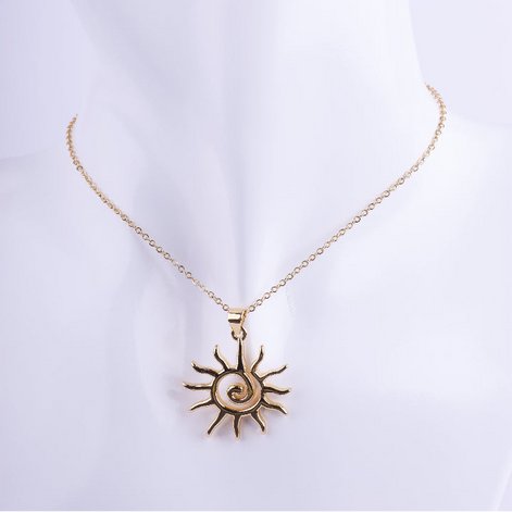 Collar de cadena de eslabones dorados finos con un dije grande de sol con rayos y una espiral pulida en el centro. El dije es de metal pulido y brillante, exhibido en un busto de maniquí blanco