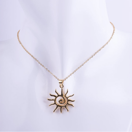 Collar de cadena de eslabones dorados finos con un dije grande de sol con rayos y una espiral pulida en el centro. El dije es de metal pulido y brillante, exhibido en un busto de maniquí blanco