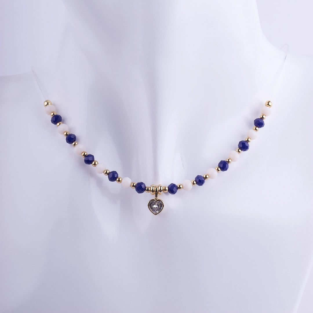 Gargantilla de cuentas facetadas en color azul zafiro y blanco nácar con separadores dorados y un dije central de corazón con zirconia. Joyería elegante bañada en oro.