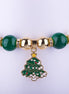 Pulsera elástica con cuentas grandes de colores verde esmeralda, blanco perlado, amarillo y rojo, con un dije esmaltado de árbol de Navidad y espaciadores dorados con cristales.