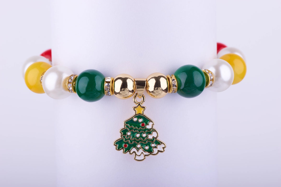 Pulsera elástica con cuentas grandes de colores verde esmeralda, blanco perlado, amarillo y rojo, con un dije esmaltado de árbol de Navidad y espaciadores dorados con cristales.