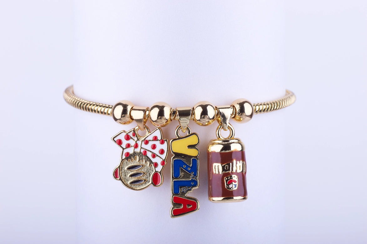 Pulsera de cadena en color oro con tres dijes esmaltados: lazo rojo con lunares, logo de Harina P.A.N. (Arepa) y lata de bebida Maltín Polar de Venezuela
