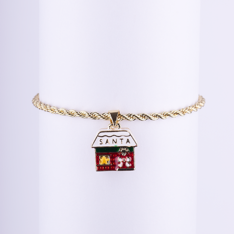 Pulsera de cadena tipo cuerda dorada con dije esmaltado de la casa o taller de Santa con detalles navideños y el texto "SANTA".