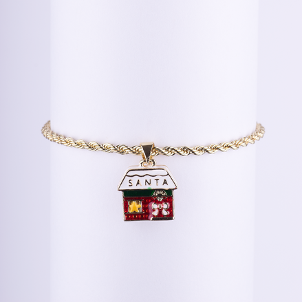 Pulsera de cadena tipo cuerda dorada con dije esmaltado de la casa o taller de Santa con detalles navideños y el texto "SANTA".