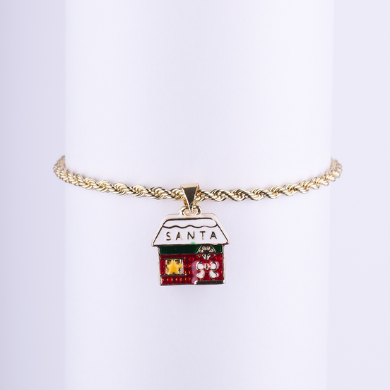 Pulsera de cadena tipo cuerda dorada con dije esmaltado de la casa o taller de Santa con detalles navideños y el texto "SANTA".