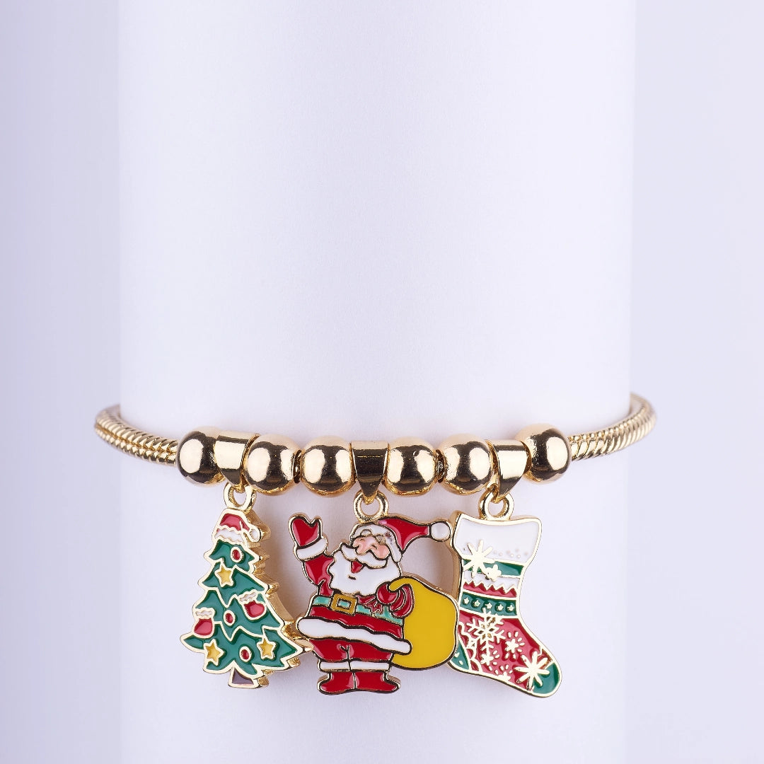 Pulsera dorada tipo brazalete con tres dijes esmaltados colgantes: Papá Noel (Santa Claus), Árbol de Navidad y Bota navideña.