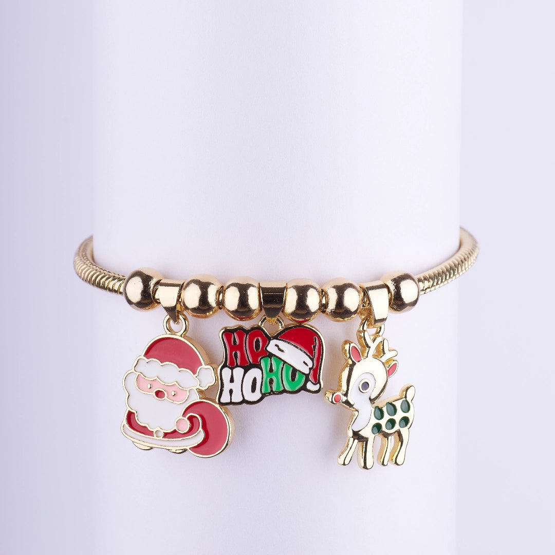 Pulsera dorada con tres dijes esmaltados colgantes: Papá Noel (Santa Claus), saludo Ho Ho Ho con gorro, y reno (ciervo) con puntos.
