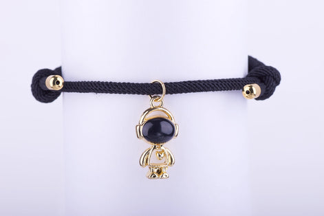 Pulsera de cuerda ajustable negra trenzada con dije de astronauta dorado y esmalte negro. Brazalete unisex de estilo urbano y moderno.