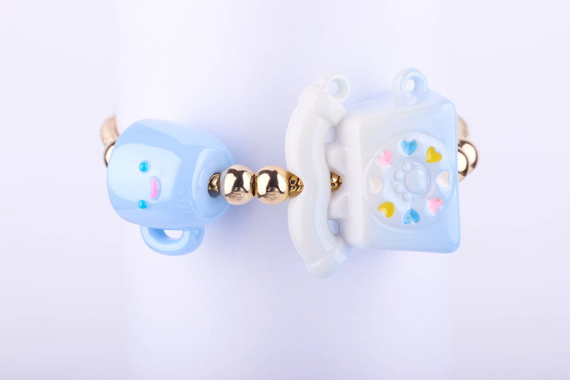 Pulsera elástica con grandes dijes de resina de teléfono fijo de disco azul pastel y taza de café azul claro. Joyería estilo kawaii con acentos dorados.