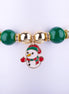 Pulsera elástica con cuentas grandes en rojo, verde y blanco perlado, dije esmaltado de muñeco de nieve con sombrero y bufanda festivos, y espaciadores dorados con cristales.