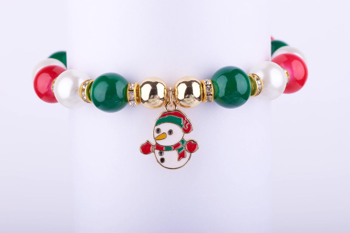 Pulsera elástica con cuentas grandes en rojo, verde y blanco perlado, dije esmaltado de muñeco de nieve con sombrero y bufanda festivos, y espaciadores dorados con cristales.