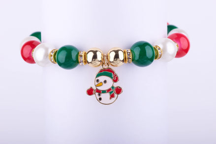 Pulsera elástica con cuentas grandes en rojo, verde y blanco perlado, dije esmaltado de muñeco de nieve con sombrero y bufanda festivos, y espaciadores dorados con cristales.