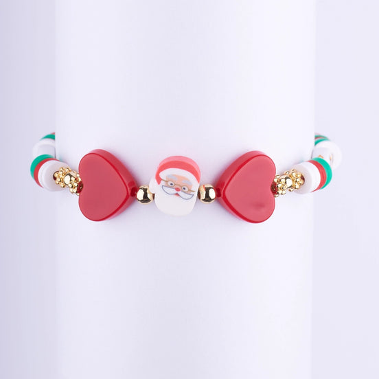 Pulsera navideña con cuentas Heishi rojas, blancas y verdes, con dos dijes grandes de corazón rojo y una cuenta central de la cara de Papá Noel.