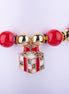 Pulsera elástica con cuentas grandes en rojo brillante y blanco perlado, espaciadores dorados con incrustaciones de cristales, y dije de caja de regalo dorada con cristales de colores.
