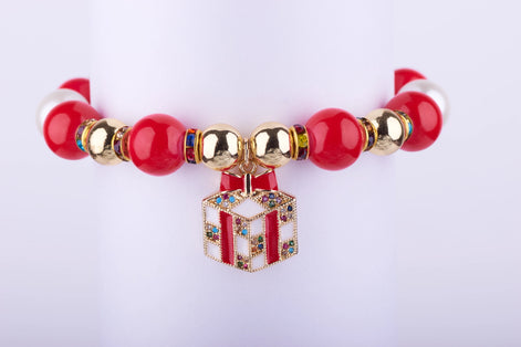 Pulsera elástica con cuentas grandes en rojo brillante y blanco perlado, espaciadores dorados con incrustaciones de cristales, y dije de caja de regalo dorada con cristales de colores.