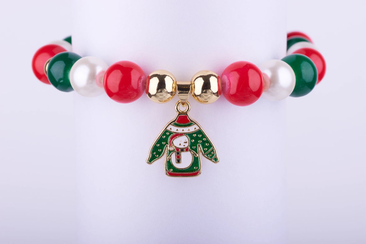 Pulsera elástica con grandes cuentas tipo perla en rojo, verde y blanco, con dije esmaltado de suéter navideño (Ugly Sweater) con diseño de muñeco de nieve.