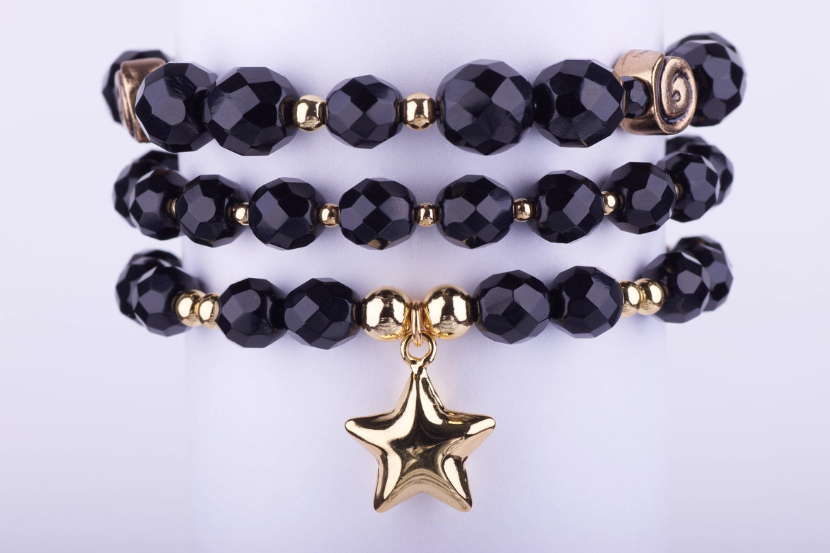 Set de 3 pulseras elásticas con cuentas de cristal facetadas en color negro brillante, separadores dorados y dije de estrella grande dorada en la pulsera inferior.